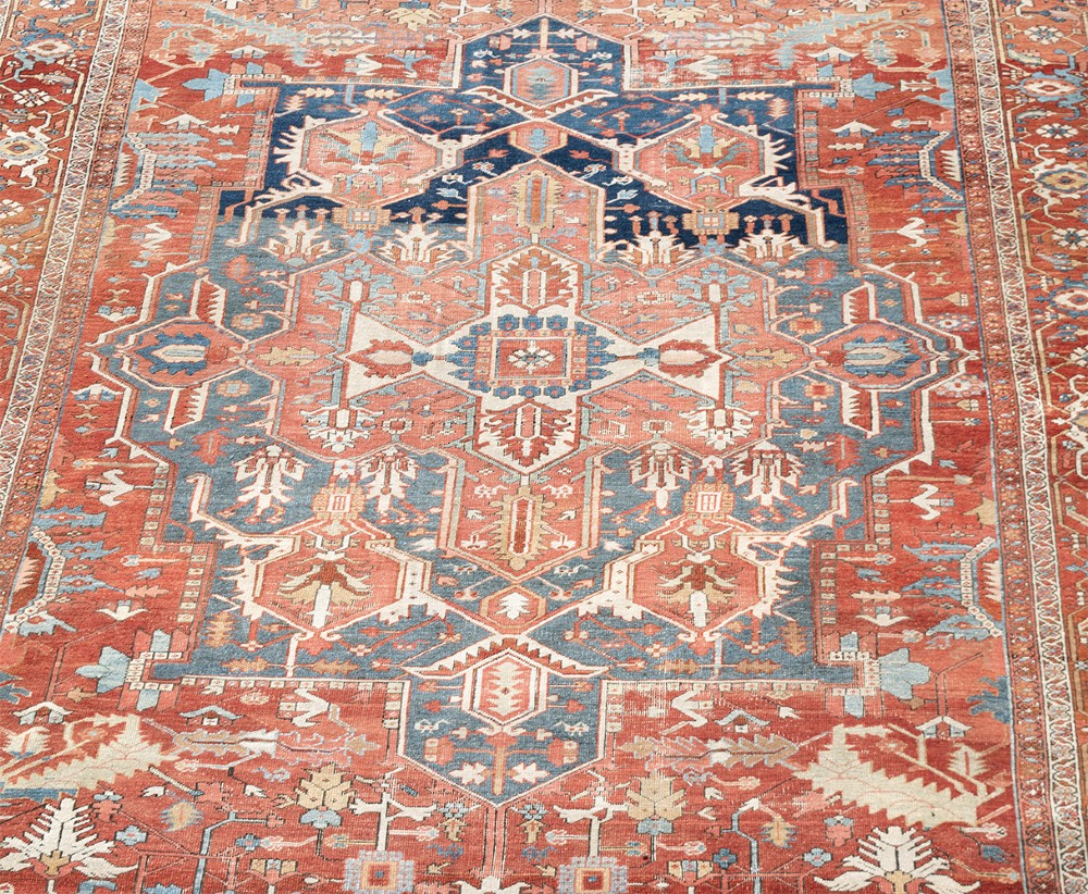 An antique Persian Heriz wool carpet featuring a bold geometric indigo medallion set against a terracotta red field with stepped spandrels and ornate borders. View IV