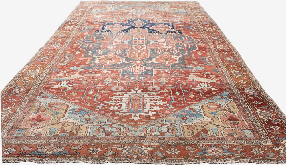 An antique Persian Heriz wool carpet featuring a bold geometric indigo medallion set against a terracotta red field with stepped spandrels and ornate borders. View V