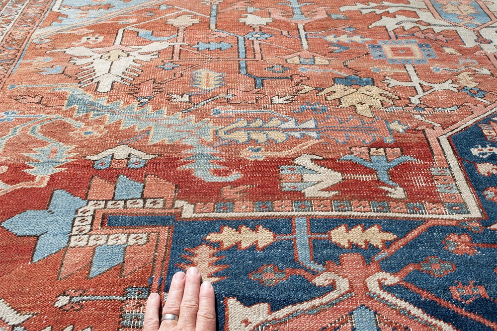 An antique Persian Heriz wool carpet featuring a bold geometric indigo medallion set against a terracotta red field with stepped spandrels and ornate borders. View VIII