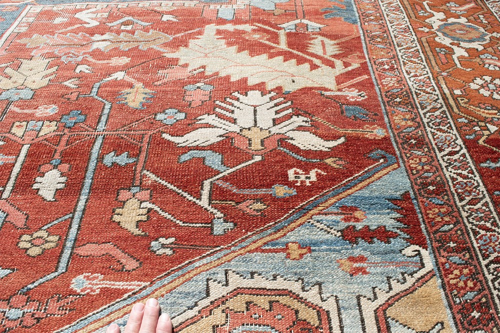 An antique Persian Heriz wool carpet featuring a bold geometric indigo medallion set against a terracotta red field with stepped spandrels and ornate borders. View IX