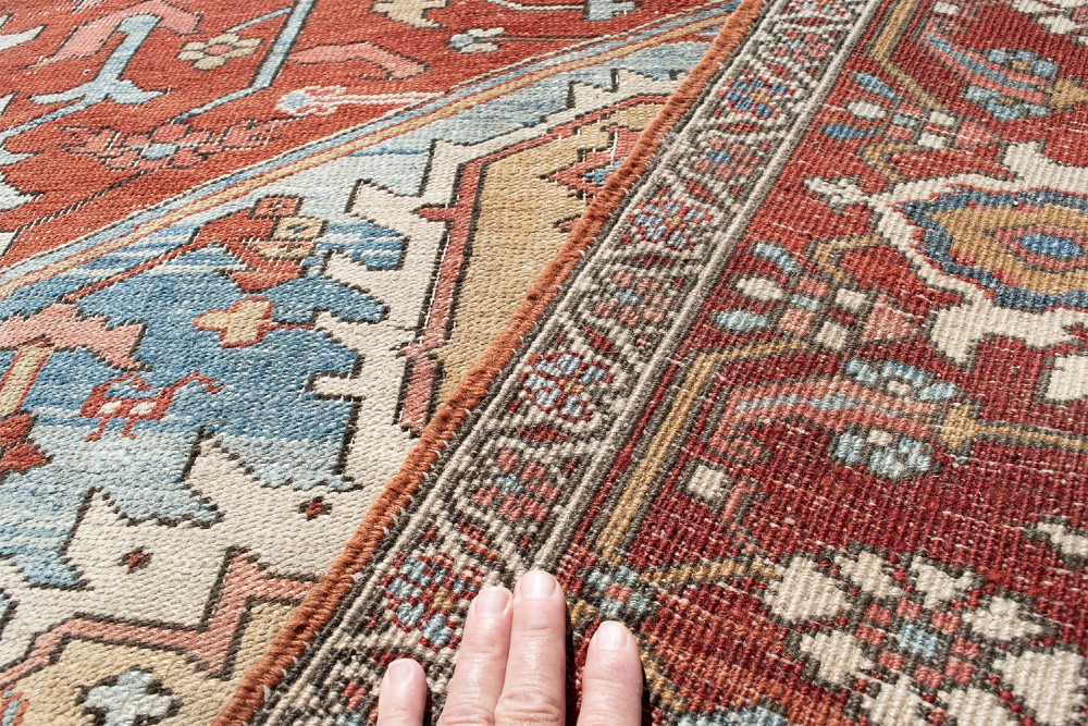 An antique Persian Heriz wool carpet featuring a bold geometric indigo medallion set against a terracotta red field with stepped spandrels and ornate borders. View XI