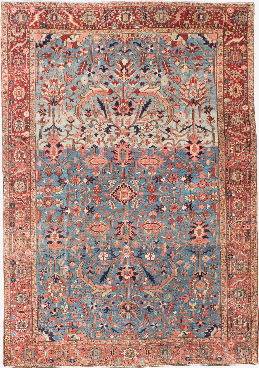 A large hand-knotted Persian Heriz wool carpet featuring a central sky blue field decorated with geometric floral motifs within a wide terracotta red border.