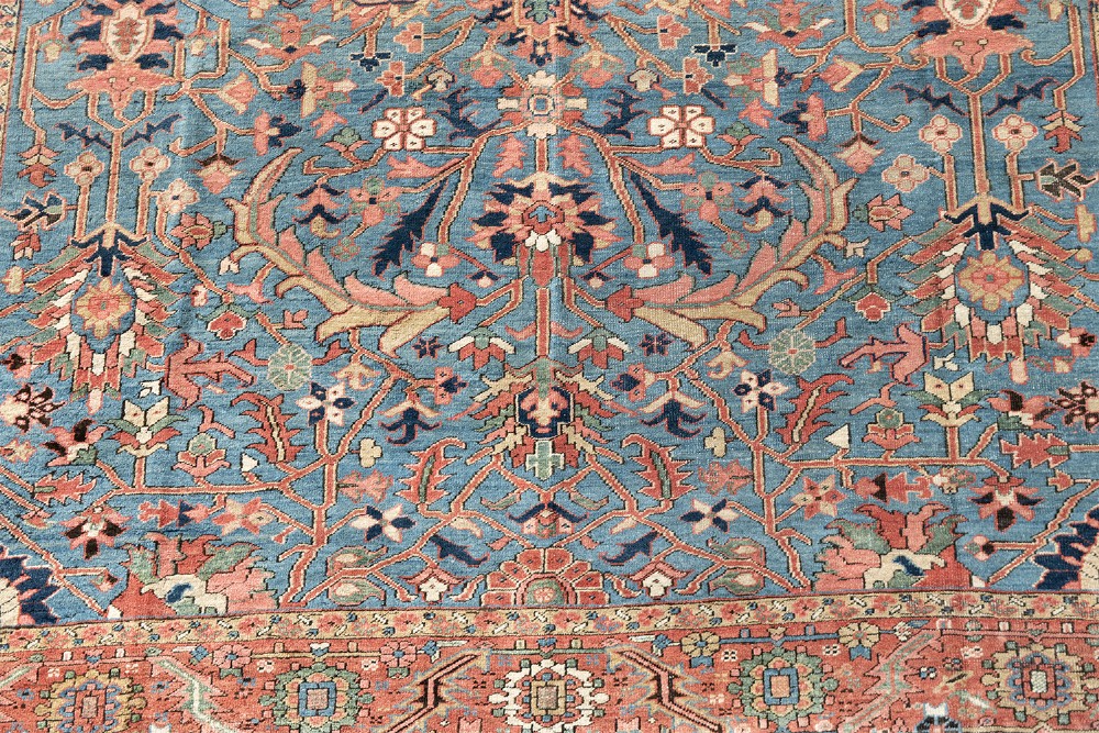 A large hand-knotted Persian Heriz wool carpet featuring a central sky blue field decorated with geometric floral motifs within a wide terracotta red border. View III