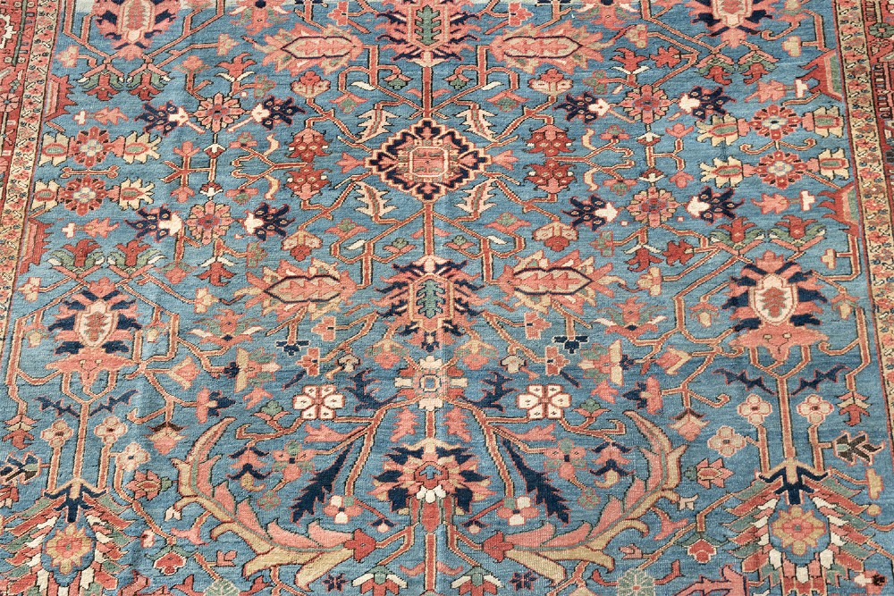 A large hand-knotted Persian Heriz wool carpet featuring a central sky blue field decorated with geometric floral motifs within a wide terracotta red border. View IV