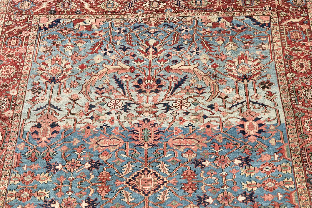 A large hand-knotted Persian Heriz wool carpet featuring a central sky blue field decorated with geometric floral motifs within a wide terracotta red border. View V