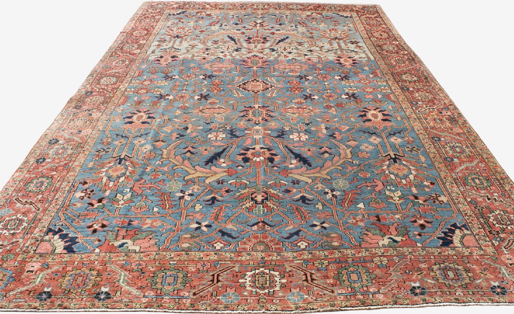 A large hand-knotted Persian Heriz wool carpet featuring a central sky blue field decorated with geometric floral motifs within a wide terracotta red border. View VI