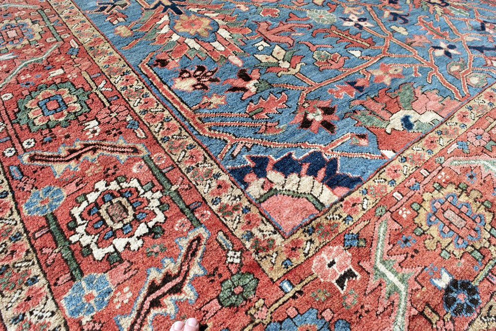 A large hand-knotted Persian Heriz wool carpet featuring a central sky blue field decorated with geometric floral motifs within a wide terracotta red border. View IX
