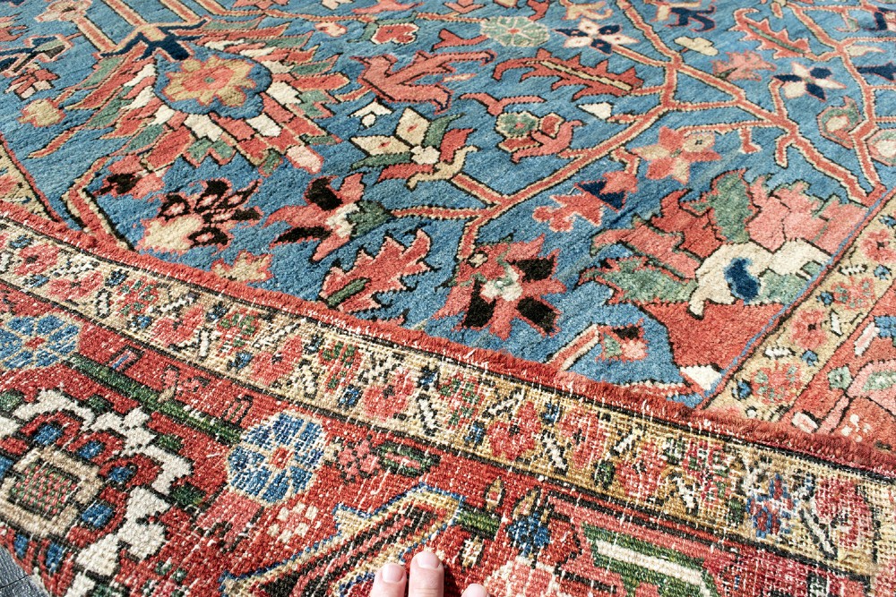 A large hand-knotted Persian Heriz wool carpet featuring a central sky blue field decorated with geometric floral motifs within a wide terracotta red border. View X