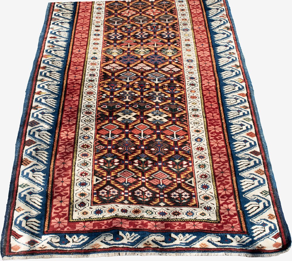 A long hand-knotted Caucasian Seychor wool rug runner featuring a dark central field with repeating geometric diamond motifs, flanked by red decorative inner borders and a blue wave pattern outer border. View II