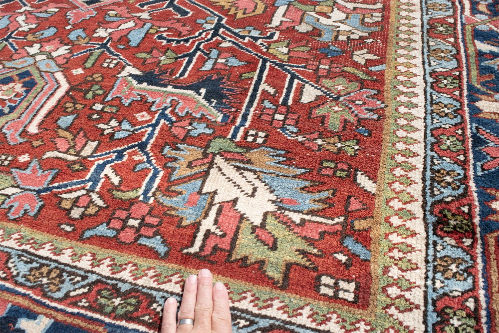 A large hand-knotted antique Persian Heriz wool carpet featuring a bold central medallion surrounded by geometric floral motifs in red, blue, green, and ivory tones. View III