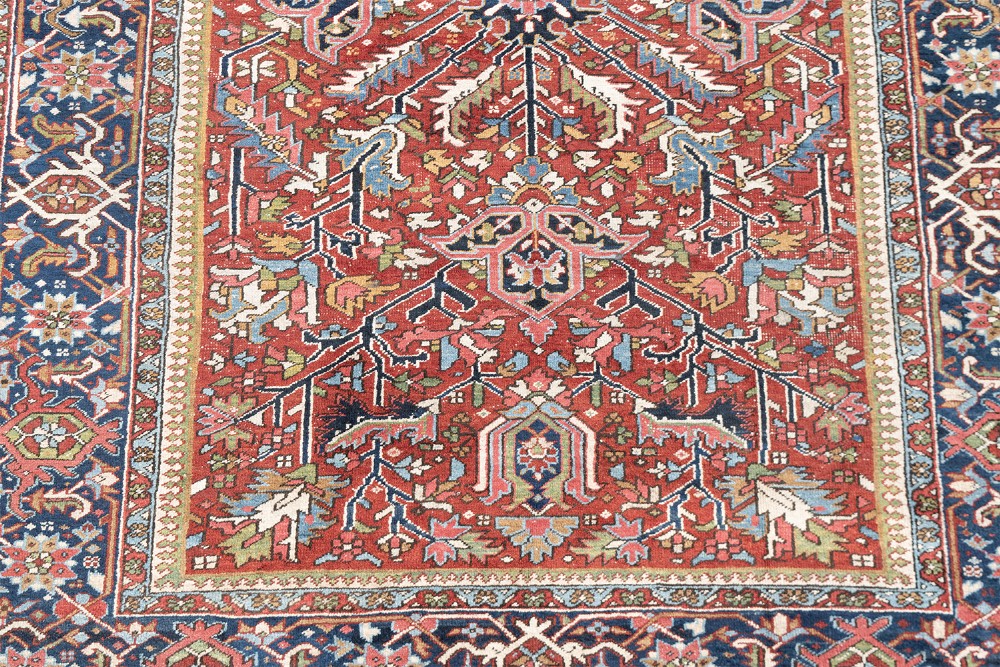 A large hand-knotted antique Persian Heriz wool carpet featuring a bold central medallion surrounded by geometric floral motifs in red, blue, green, and ivory tones. View VII