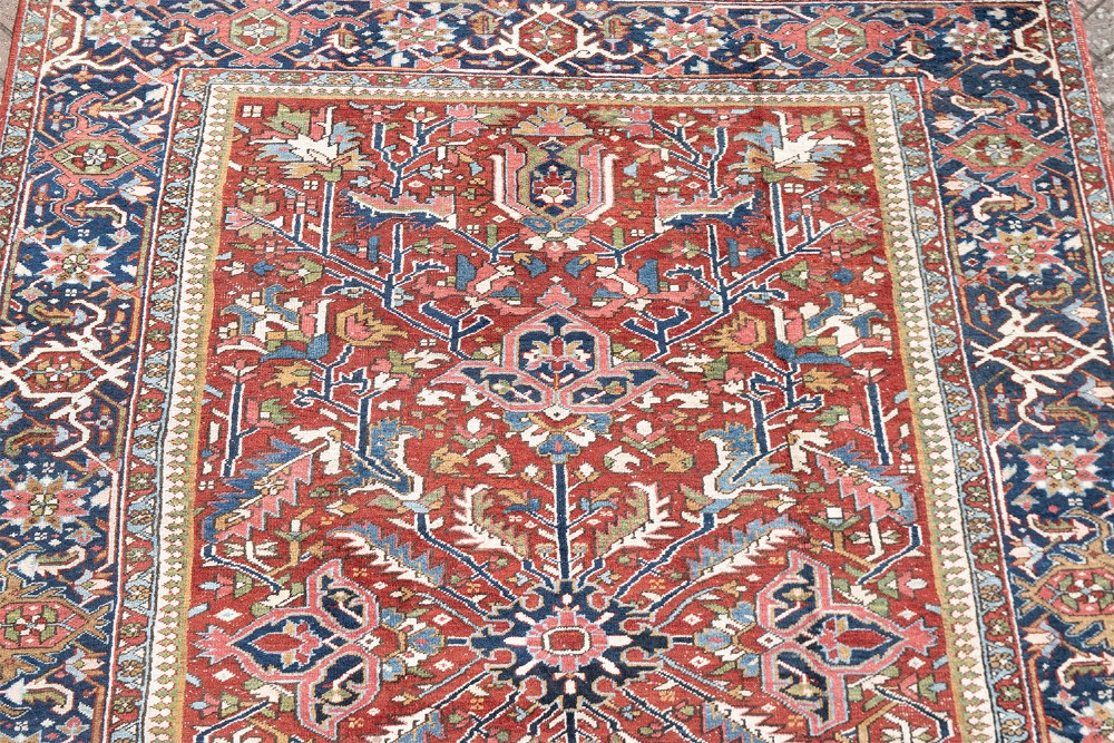 A large hand-knotted antique Persian Heriz wool carpet featuring a bold central medallion surrounded by geometric floral motifs in red, blue, green, and ivory tones. View VIII