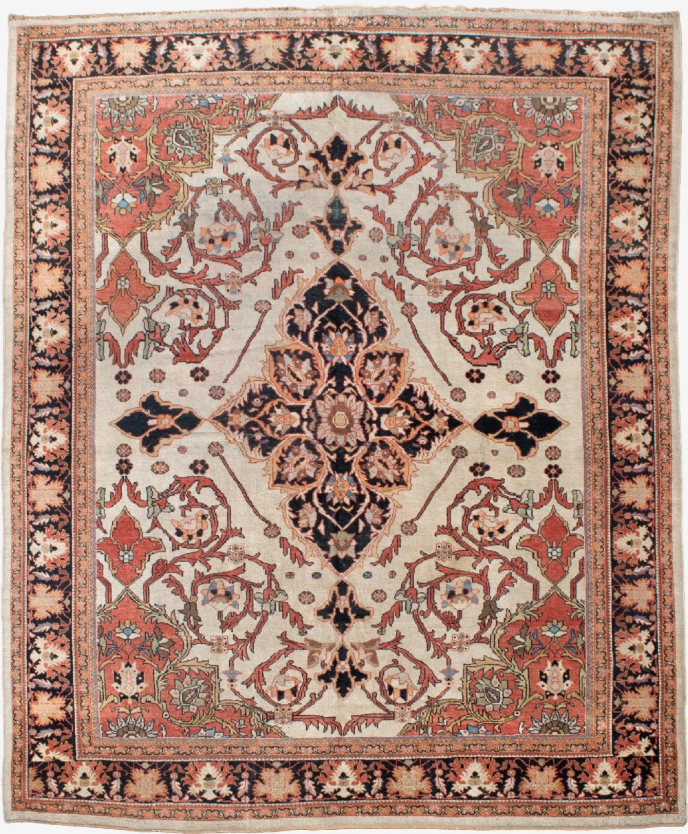 A large hand-knotted antique Mahal Persian carpet featuring a central dark blue floral medallion on an ivory field framed by terracotta spandrels and a multi-tiered border.