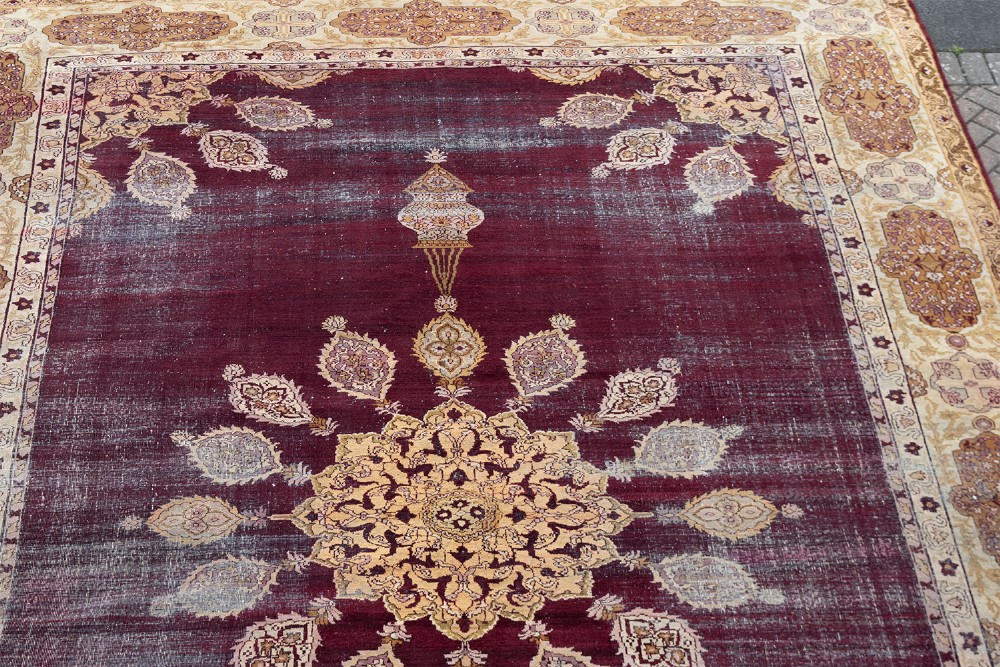A large hand-knotted wool carpet featuring a central starburst medallion surrounded by floral motifs on a deep magenta field with a broad cream patterned border. View III