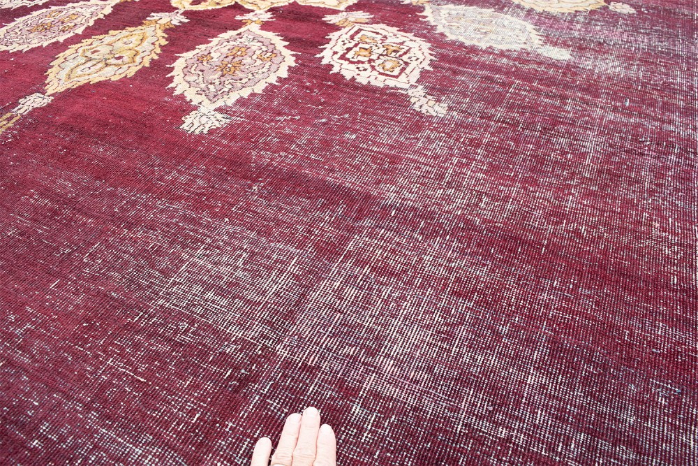 A large hand-knotted wool carpet featuring a central starburst medallion surrounded by floral motifs on a deep magenta field with a broad cream patterned border. View V