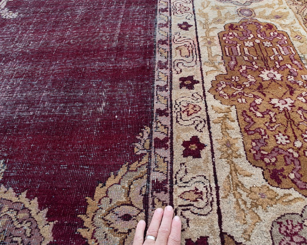 A large hand-knotted wool carpet featuring a central starburst medallion surrounded by floral motifs on a deep magenta field with a broad cream patterned border. View VI