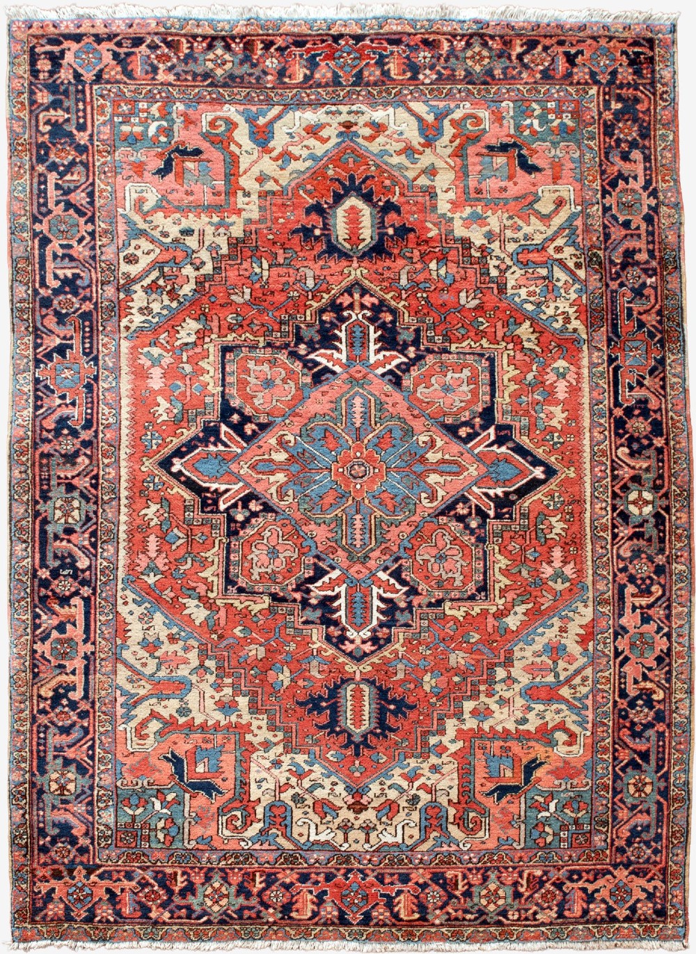 An antique Persian Heriz wool carpet with a large central geometric medallion in terracotta, navy blue, and light blue against an ivory and red field.