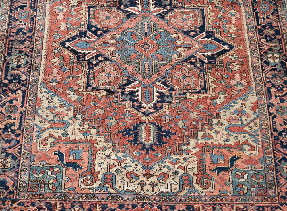 An antique Persian Heriz wool carpet with a large central geometric medallion in terracotta, navy blue, and light blue against an ivory and red field. View III