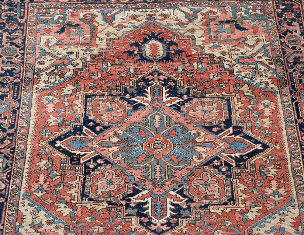 An antique Persian Heriz wool carpet with a large central geometric medallion in terracotta, navy blue, and light blue against an ivory and red field. View IV