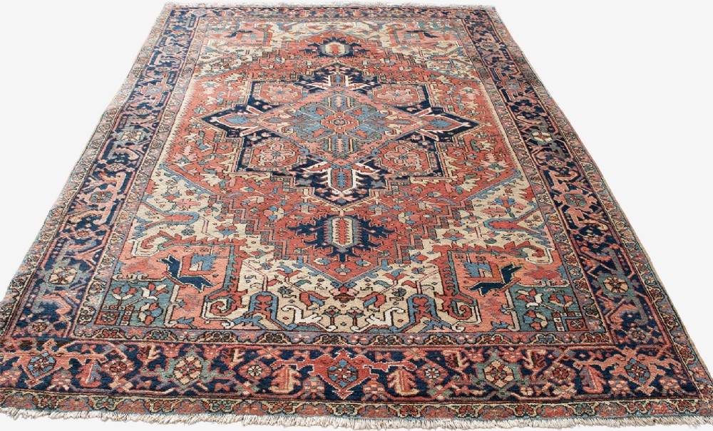 An antique Persian Heriz wool carpet with a large central geometric medallion in terracotta, navy blue, and light blue against an ivory and red field. View V