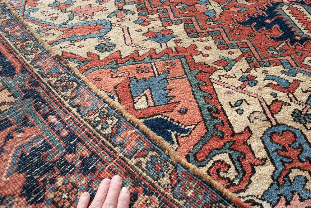 An antique Persian Heriz wool carpet with a large central geometric medallion in terracotta, navy blue, and light blue against an ivory and red field. View VII
