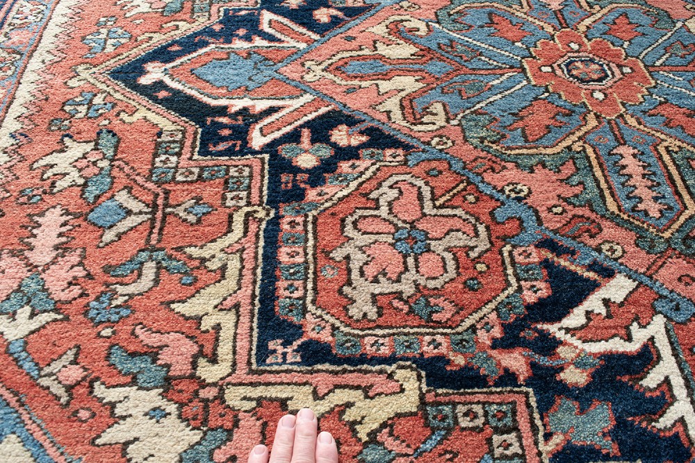 An antique Persian Heriz wool carpet with a large central geometric medallion in terracotta, navy blue, and light blue against an ivory and red field. View VIII