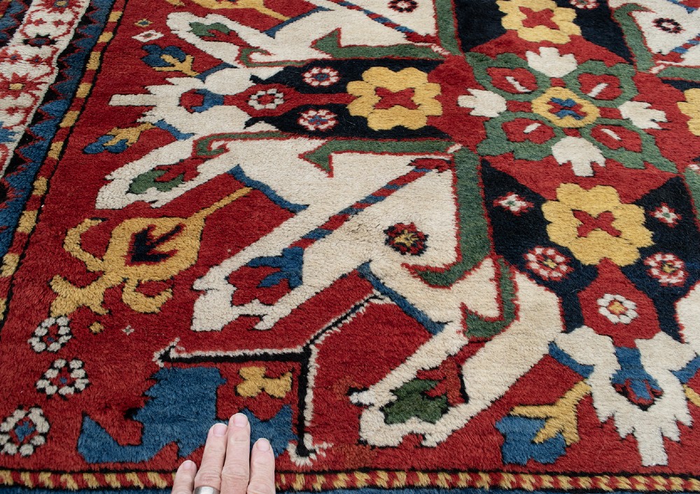 An antique hand-knotted Caucasian Eagle Kazak wool rug featuring repeating ivory geometric eagle medallions on a vibrant red field with a patterned border. View III