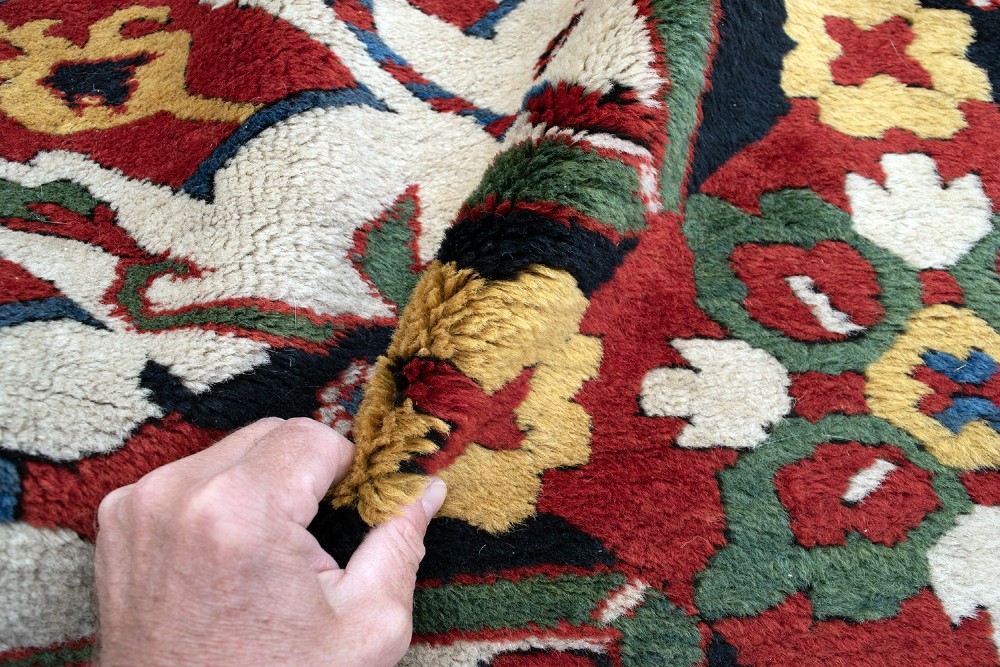 An antique hand-knotted Caucasian Eagle Kazak wool rug featuring repeating ivory geometric eagle medallions on a vibrant red field with a patterned border. View V