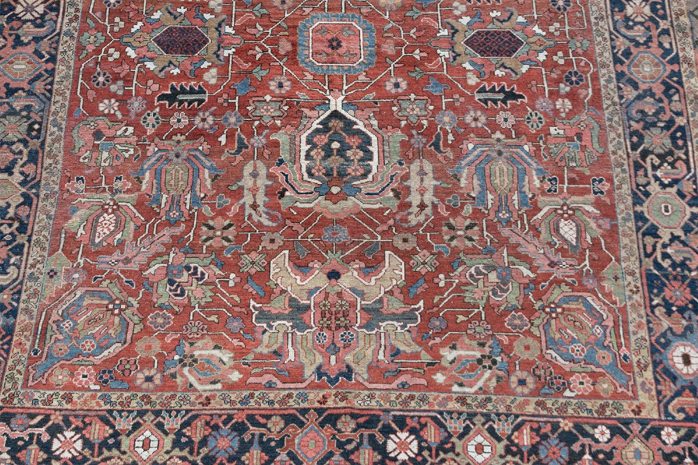 An antique Persian Heriz wool carpet featuring a central geometric medallion on a terracotta field surrounded by a dark navy decorative border. View II