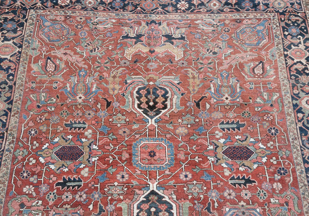 An antique Persian Heriz wool carpet featuring a central geometric medallion on a terracotta field surrounded by a dark navy decorative border. View III