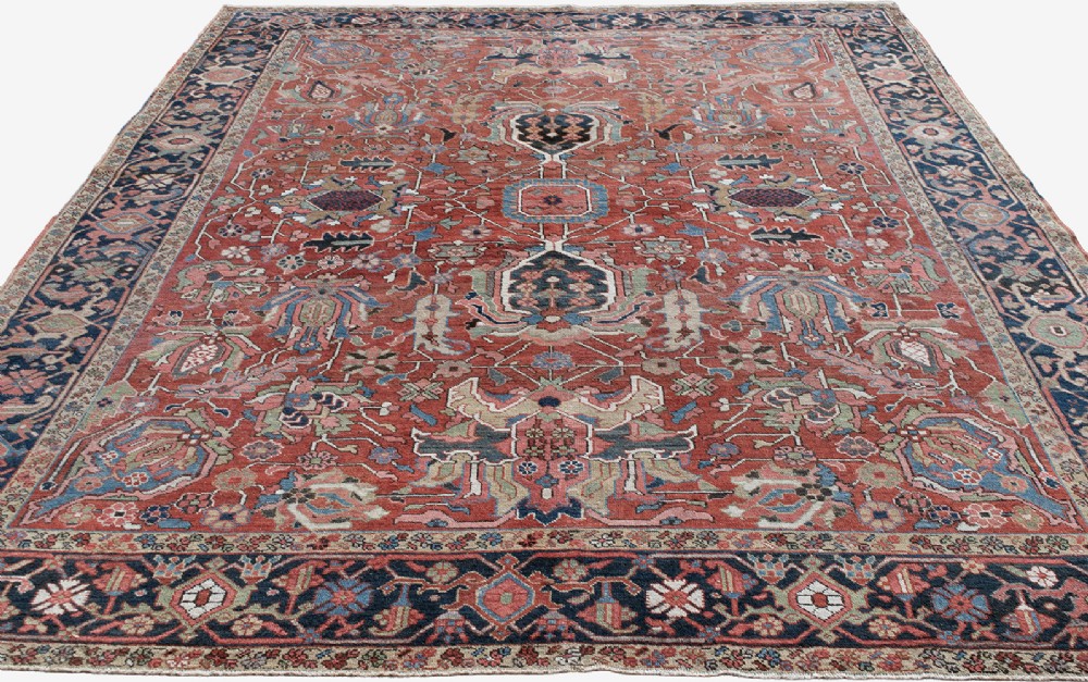 An antique Persian Heriz wool carpet featuring a central geometric medallion on a terracotta field surrounded by a dark navy decorative border. View IV
