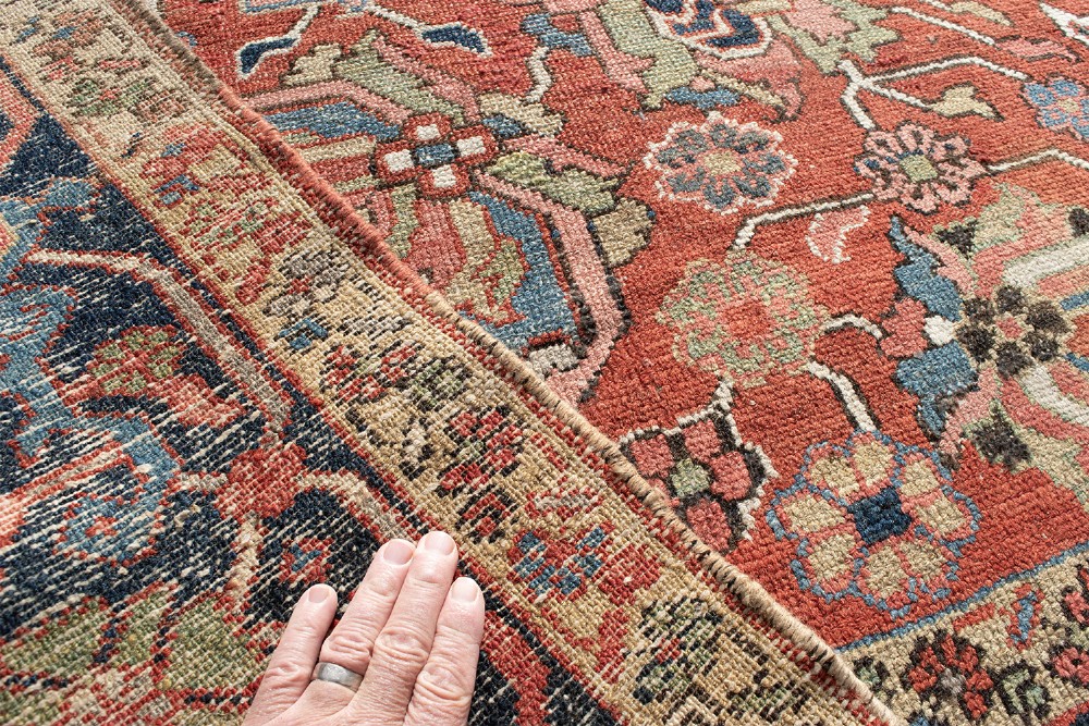 An antique Persian Heriz wool carpet featuring a central geometric medallion on a terracotta field surrounded by a dark navy decorative border. View IX