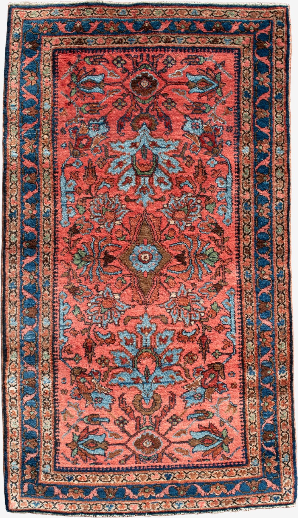 A small rectangular hand-knotted wool rug featuring a coral-red central field decorated with blue and brown floral motifs surrounded by a dark blue border.