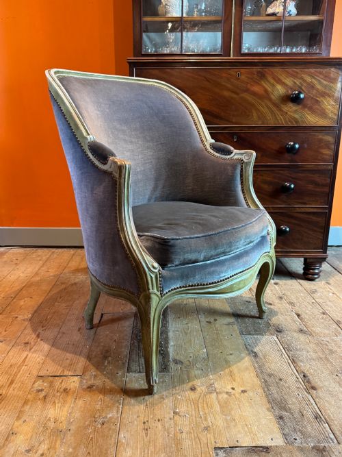 fig 1. An antique Louis XV style tub bergere armchair upholstered in slate grey velvet with a carved distressed green wooden frame and cabriole legs.