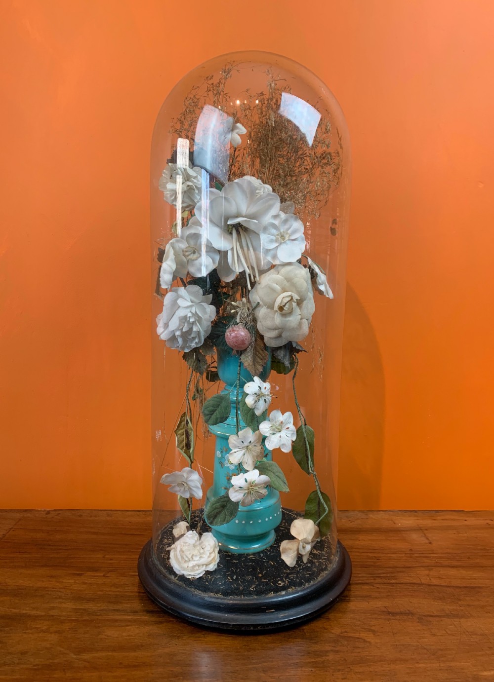 A tall Victorian glass dome containing a glass vase of faux flowers