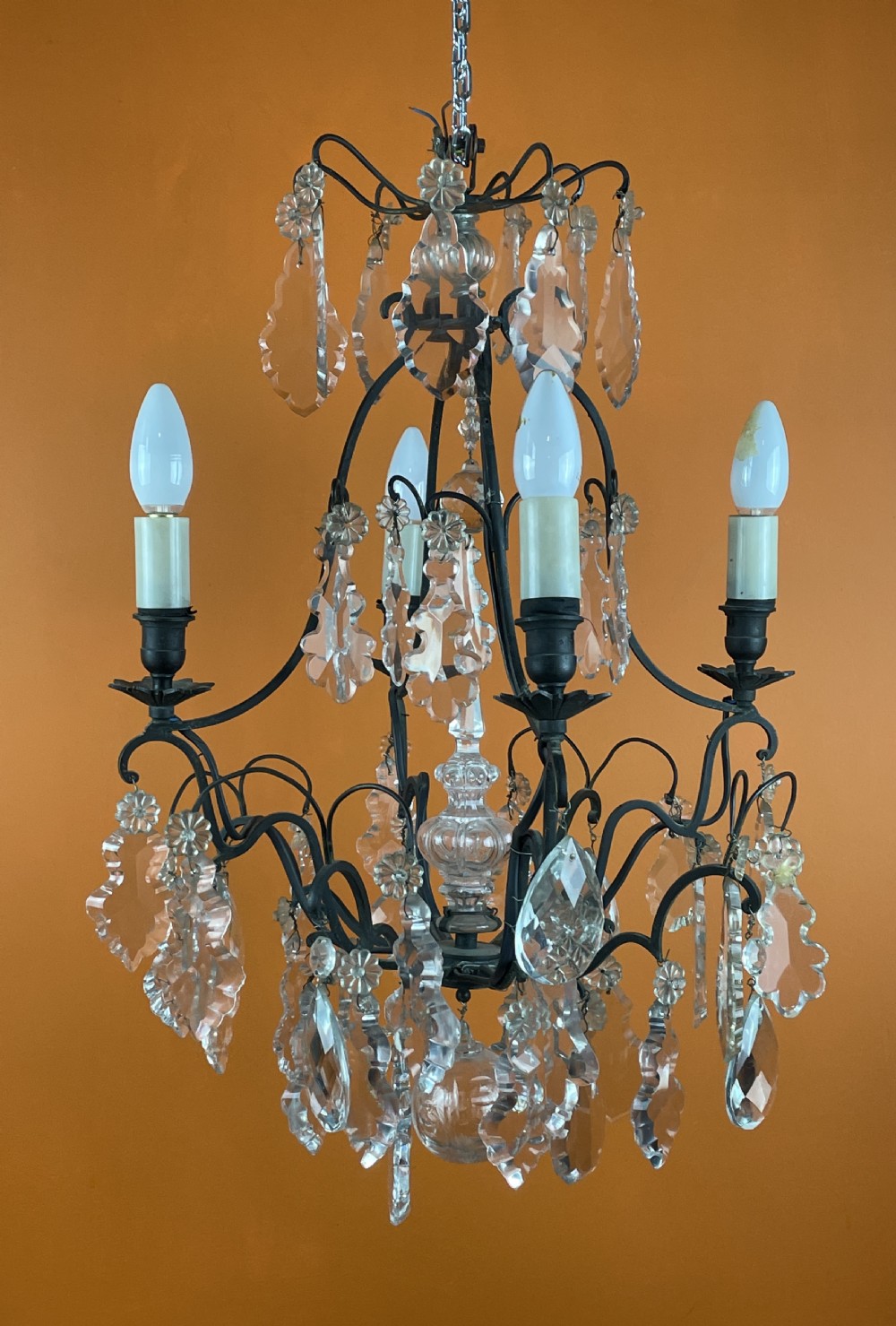 A French style cut glass cage chandelier featuring a dark wrought iron frame decorated with clear glass drops, rosettes, and candle-style bulb sockets.