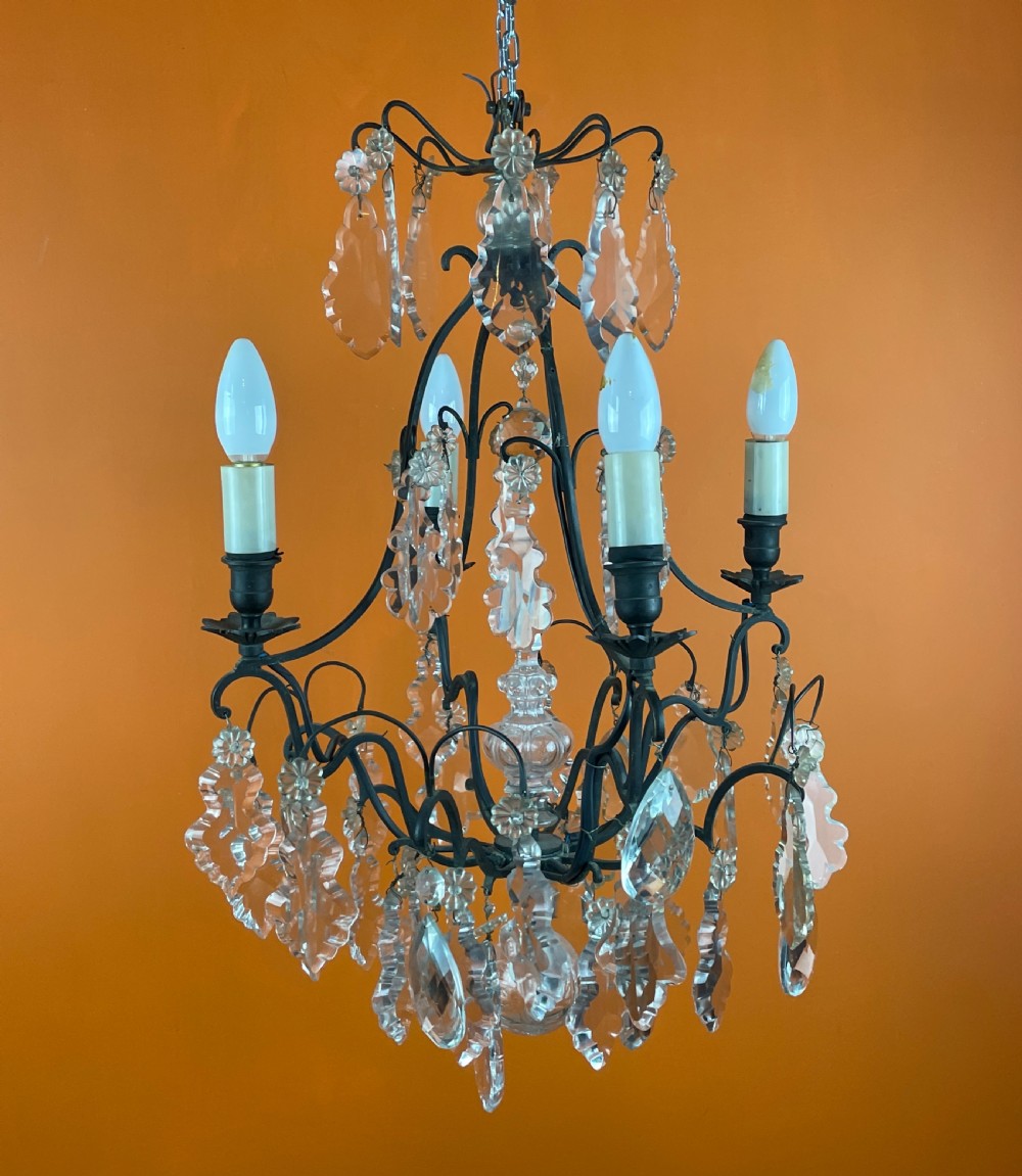 A French style cut glass cage chandelier featuring a dark wrought iron frame decorated with clear glass drops, rosettes, and candle-style bulb sockets. View IV