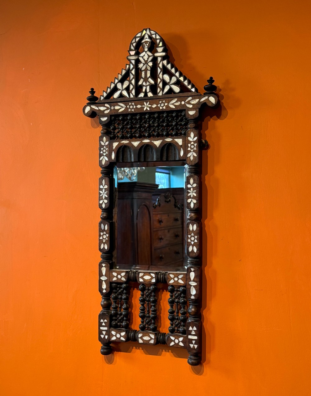 A tall dark walnut wall mirror decorated with mother-of-pearl geometric inlays, turned wooden spindles, and an arched cresting pediment.