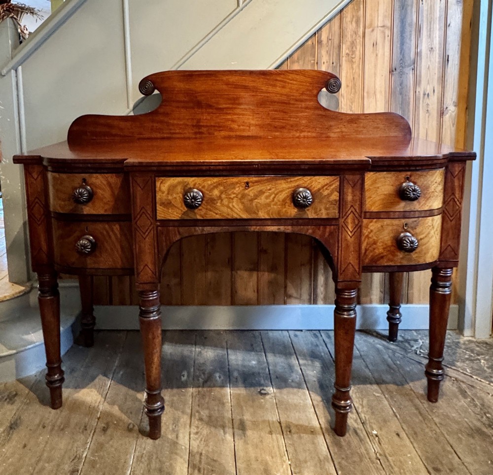 A small Regency mahogany sideboard featuring ebony stringing, turned legs, a raised scroll gallery backboard, and five drawers with turned wooden knobs.