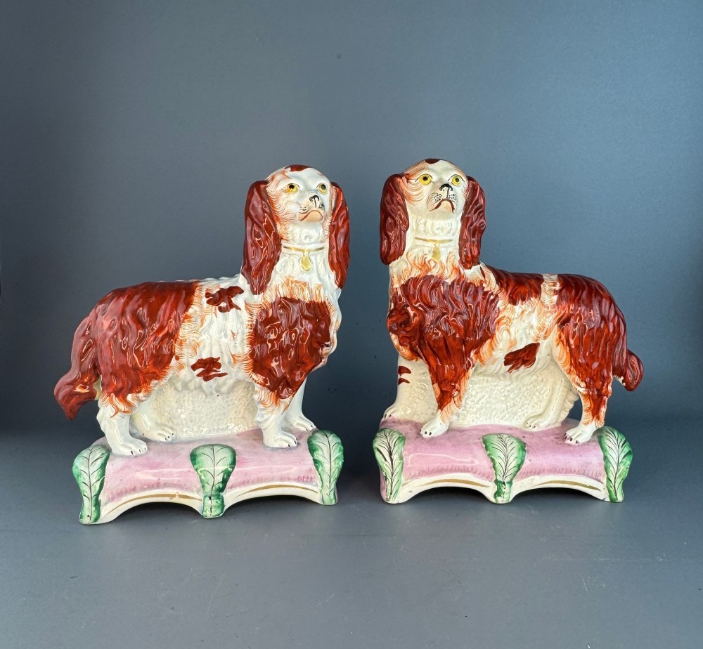 A pair of 19th-century Victorian Staffordshire earthenware spaniel dogs painted in russet brown and white standing on pink cushion bases.