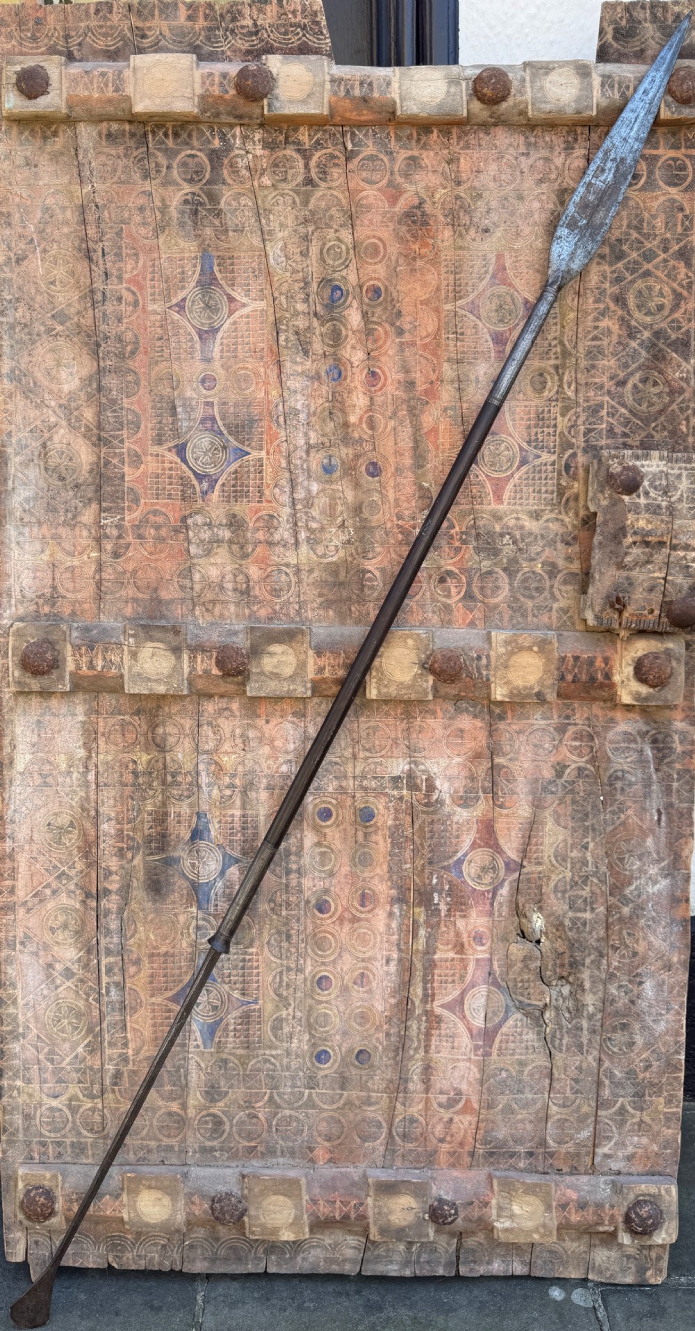 A hand-forged dark steel spearhead with a defined central ridge attached to a slender wooden shaft. View III