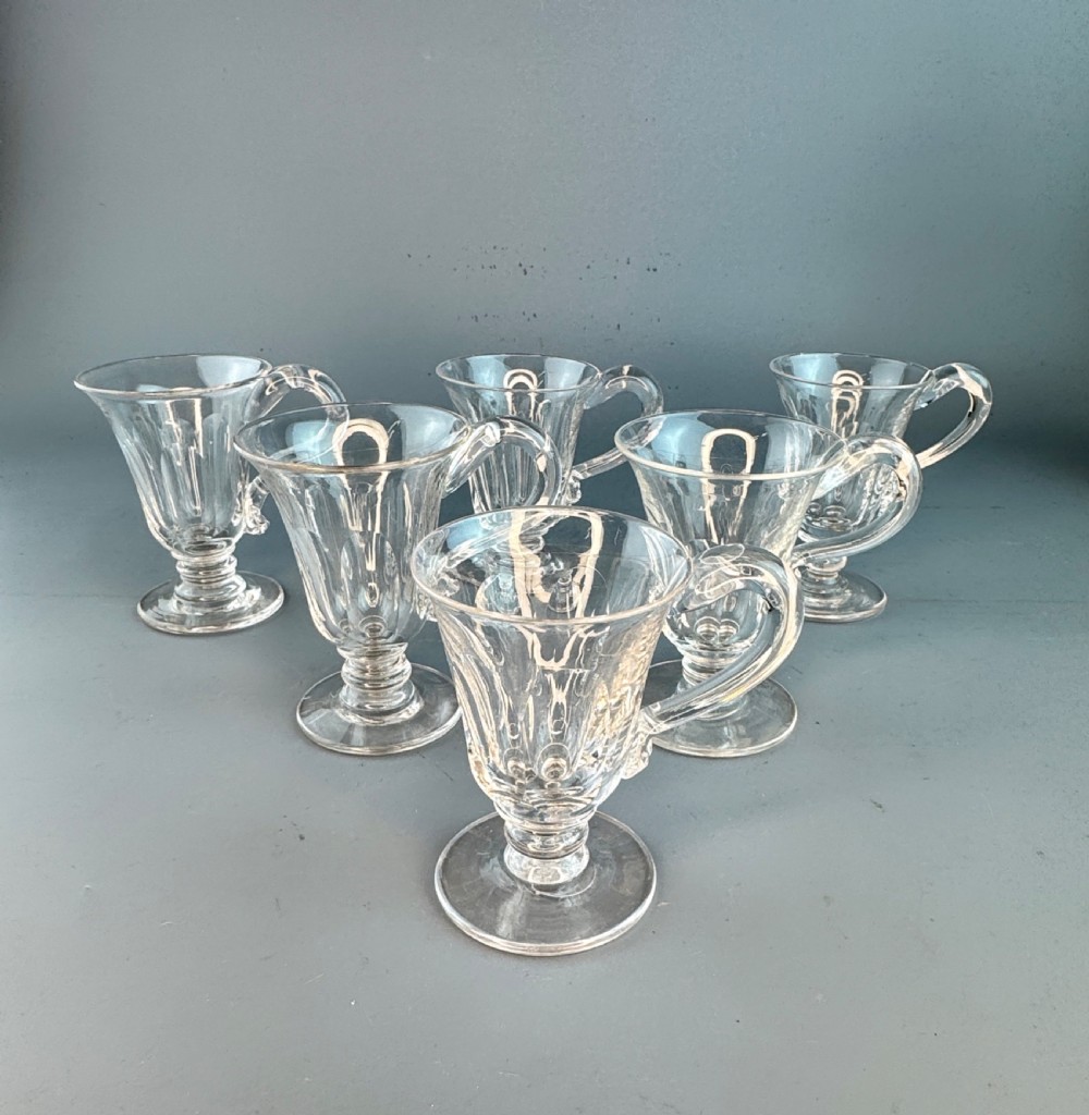 A set of six early Victorian clear cut glass custard cups featuring fluted bowls, pedestal bases, and loop handles.