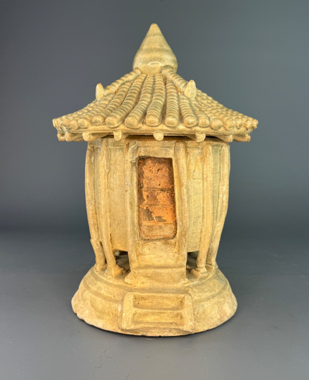 A pale celadon glazed ceramic granary model featuring a ribbed cylindrical body, rectangular doorway aperture, and a tiled pagoda roof topped with a pointed finial.