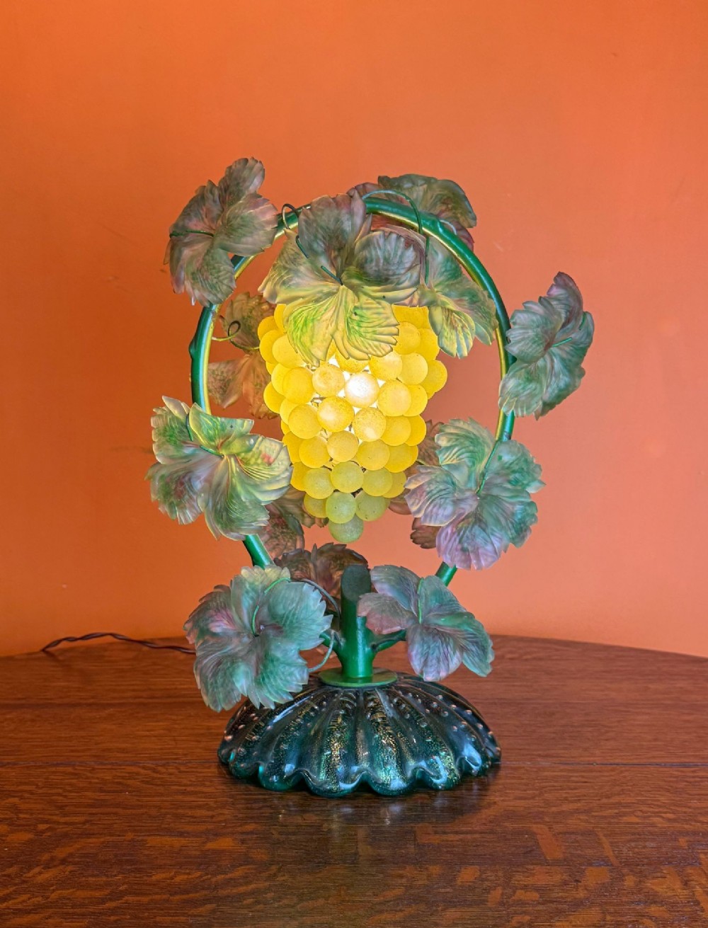 A vintage Italian Murano glass table lamp shaped as a cluster of yellow grapes surrounded by green frosted glass leaves and a ribbed green base.