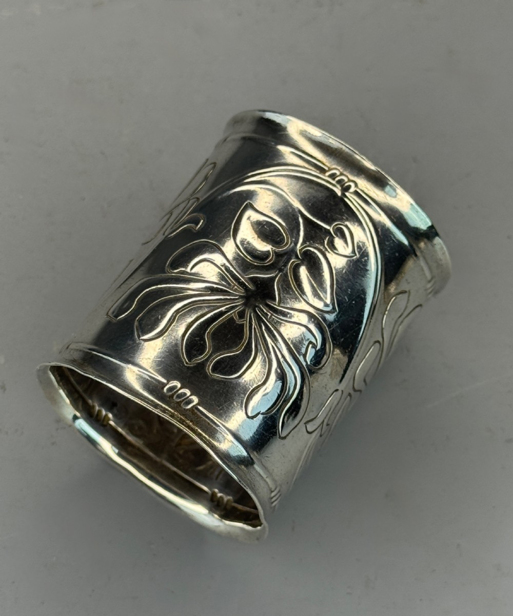 A cylindrical silver napkin ring decorated with raised Art Nouveau floral motifs and stylized whiplash foliage.