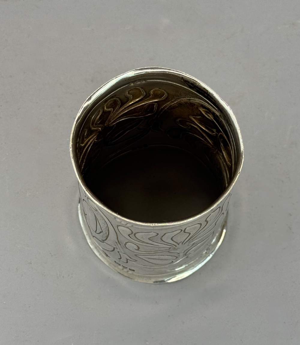 A cylindrical silver napkin ring decorated with raised Art Nouveau floral motifs and stylized whiplash foliage. View III