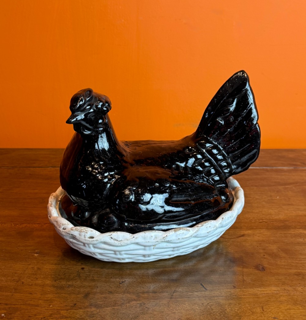A Victorian Staffordshire Jackfield ceramic covered dish featuring a black glazed hen resting atop a white basketweave earthenware base.