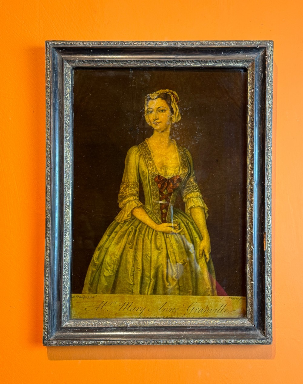 An 18th-century reverse glass mezzotint portrait depicting a woman in a yellow dress set within a dark moulded frame.