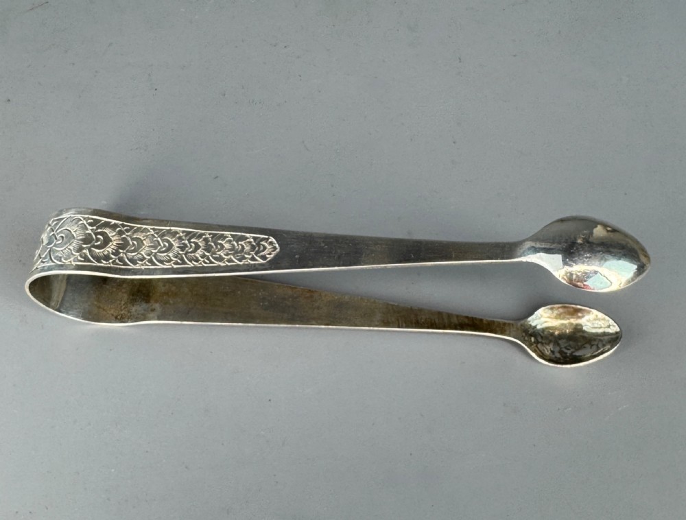 A pair of silver sugar tongs featuring textured engraved decoration near the arch and spoon-shaped bowls. View II