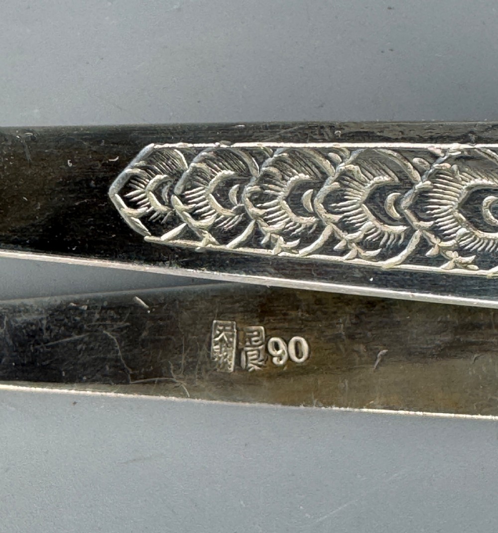 A pair of silver sugar tongs featuring textured engraved decoration near the arch and spoon-shaped bowls. View III